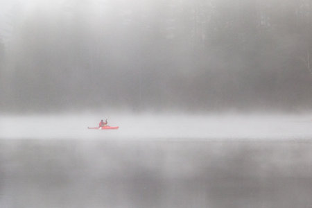 Kayaker in red gear paddling in fog on quiet lakeの写真素材