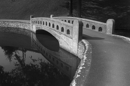 Black and white curved cement arch bridge over water for pedestrians