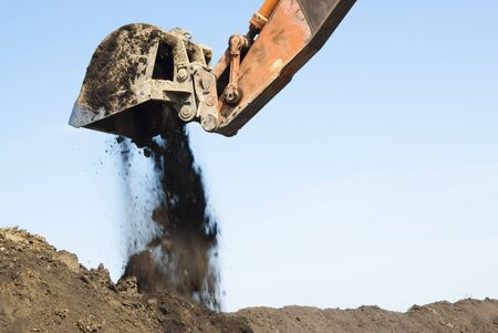 an excavator dumping a bucket of dirtの写真素材
