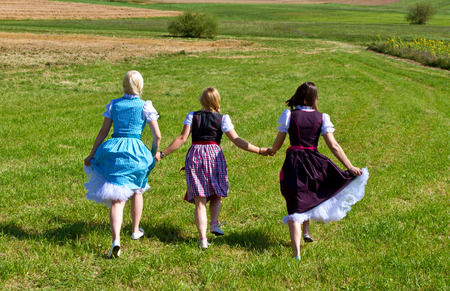Three girls in dirndl running over a meadowの写真素材