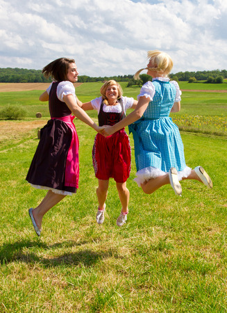 Girls in dirndls jumping on a meadowの写真素材