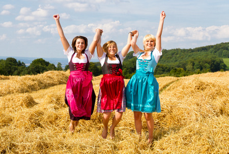 Three girls in dirndl having fun on a fieldの写真素材