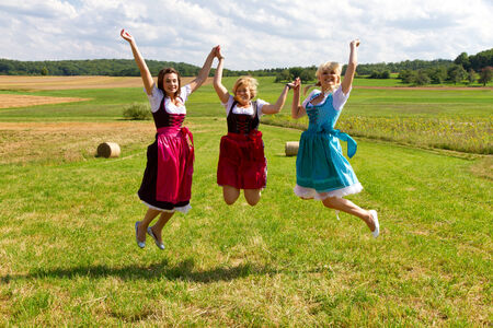 Three girls in dirndl jumping in the airの写真素材