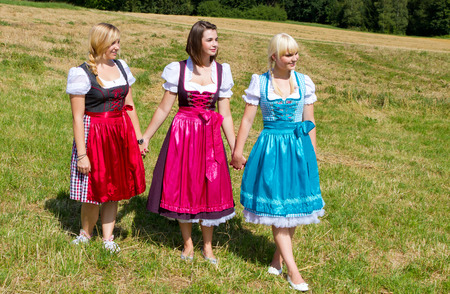 Three girls in colorful dirndl walking on a meadowの写真素材