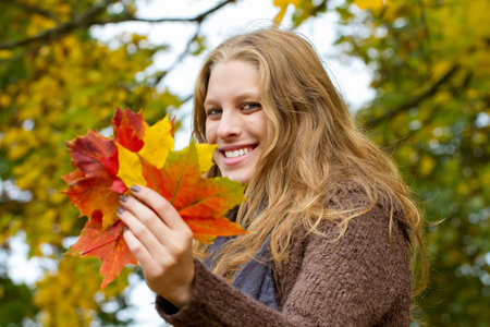 Young blond woman with autumn leaves in hand