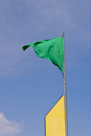 A green flag waving in a yellow mast authorize bathing in the beach.の写真素材
