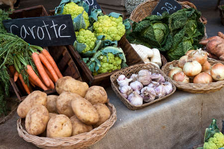 Vegetables for sell in vintage french street market. Potatoes, carrots,green cauliflower,garlic, onions and cabbage in wood and osier baskets.の写真素材