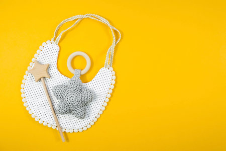 Bibs and wooden toys. A set of children's things and accessories for a girl on a yellow background. The concept of children's soul. fashion newborn baby. Flat bed, top view.の写真素材
