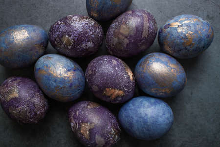 Easter card with a copy of the place for the text. Purple, blue and golden eggs on a dark background. The trend of 2022 purple shade is very peri. Natural dye karkade tea. Top view.の写真素材