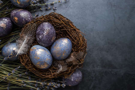 Easter card with a copy of the place for the text. Purple, blue and golden eggs with lavender on a dark background. The purple hue trend of 2022 is very relevant. Natural dye karkade tea. top view.の写真素材