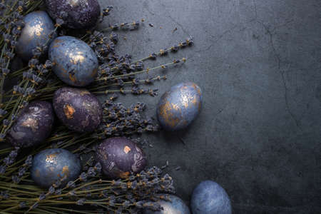 Easter card with a copy of the place for the text. Purple, blue and golden eggs with lavender on a dark background. The purple hue trend of 2022 is very relevant. Natural dye karkade tea. top view.の写真素材
