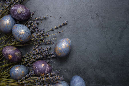 Easter card with a copy of the place for the text. Purple, blue and golden eggs with lavender on a dark background. The purple hue trend of 2022 is very relevant. Natural dye karkade tea. top view.の写真素材