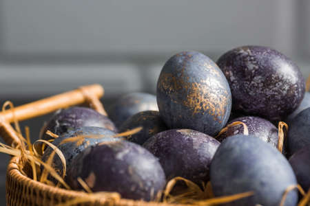Easter card with a copy of the place for the text. Purple, blue and golden eggs in a basket on a dark background. The purple hue trend of 2022 is very peri. Natural dye karkade tea. top view.の写真素材