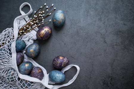 Easter card with a copy of the place for the text. Purple, blue and golden eggs in a string bag on a dark background. The trend of 2022 purple shade is very peri. Natural dye karkade tea. Top view.の写真素材