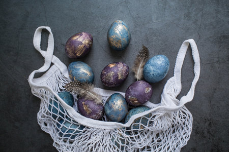 Easter card with a copy of the place for the text. Purple, blue and golden eggs in a string bag on a dark background. The trend of 2022 purple shade is very peri. Natural dye karkade tea. Top view.の写真素材
