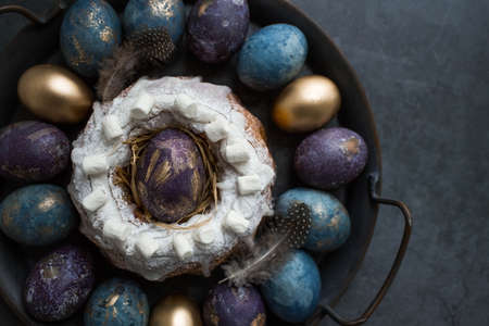 Easter card with a copy of the place for the text. Purple, blue and golden eggs with a cake on a dark background. The purple hue trend of 2022 is very peri. Natural dye karkade tea. top view.の写真素材