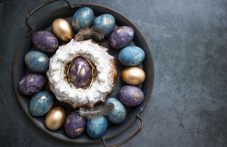 Easter card with a copy of the place for the text. Purple, blue and golden eggs with a cake on a dark background. The purple hue trend of 2022 is very peri. Natural dye karkade tea. top view.の写真素材