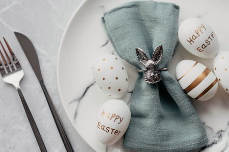Banner. table settings. A fashionable marble plate with a rabbit on a napkin, Easter eggs and feathers on a gray background. top view. Happy Easter holiday concept for cafes and restaurants.の写真素材