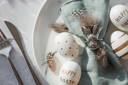 Banner. table settings. A fashionable marble plate with a rabbit on a napkin, Easter eggs and feathers on a gray background. top view. Happy Easter holiday concept for cafes and restaurants.の写真素材