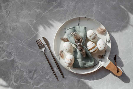 Banner. table settings. A fashionable marble plate with a rabbit on a napkin, Easter eggs and feathers on a gray background. top view. Happy Easter holiday concept for cafes and restaurants.の写真素材
