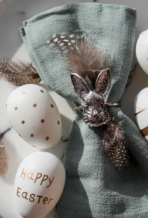 Banner. table settings. A fashionable marble plate with a rabbit on a napkin, Easter eggs and feathers on a gray background. top view. Happy Easter holiday concept for cafes and restaurants.の写真素材