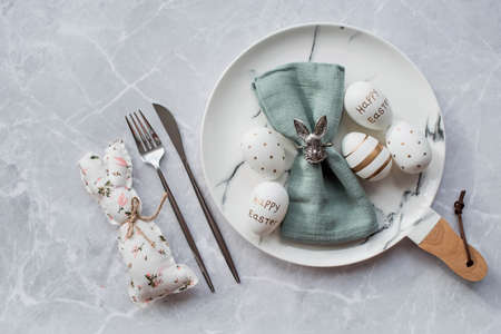 Banner. table settings. A fashionable marble plate with a rabbit on a napkin, Easter eggs and feathers on a gray background. top view. Happy Easter holiday concept for cafes and restaurants.の写真素材