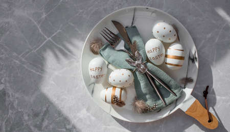 Banner. table settings. A fashionable marble plate with a rabbit on a napkin, Easter eggs and feathers on a gray background. top view. Happy Easter holiday concept for cafes and restaurants.の写真素材