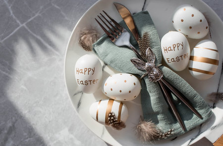 Banner. table settings. A fashionable marble plate with a rabbit on a napkin, Easter eggs and feathers on a gray background. top view. Happy Easter holiday concept for cafes and restaurants.の写真素材