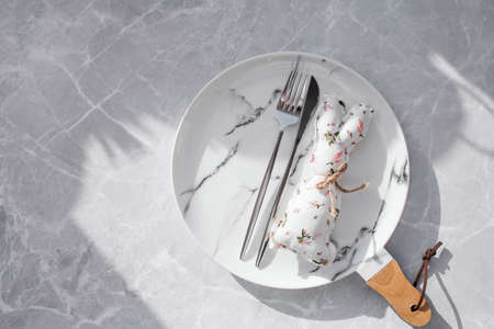 Banner. table setting. A fashionable marble plate with a rabbit on a napkin, Easter eggs and feathers on a gray background. top view. Happy Easter holiday concept for cafes and restaurants.の写真素材