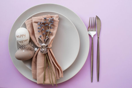 Banner. table setting. A plate with a rabbit on a napkin, lavender and Easter eggs on a fashionable background of 2022 is a veri pery. top view. The concept of a happy Easter holiday for cafes.の写真素材