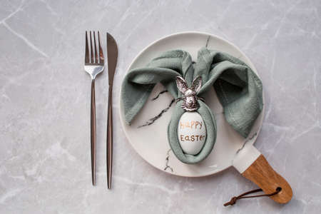 Banner. table setting. A fashionable marble plate with a rabbit and an egg in a napkin on a gray background. top view. Happy Easter holiday concept for cafes and restaurants.の写真素材