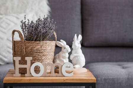 Provence. A wicker basket with a bouquet of lavender and white rabbits in the interior of the living room on a wooden table. The concept of home comfort in the bright holiday of Easter 2022.の写真素材