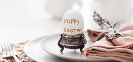 table setting. A plate of Easter eggs, rabbits, lavender and a napkin with appliances on a white table. There is a Scandinavian-style kitchen in the background. The concept of a bright Easter holiday.の写真素材