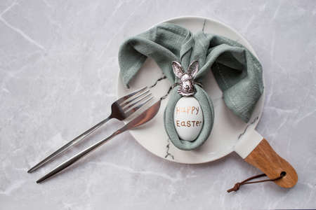 Banner. table setting. A fashionable marble plate with a rabbit and an egg in a napkin on a gray background. top view. Happy Easter holiday concept for cafes and restaurants.の写真素材