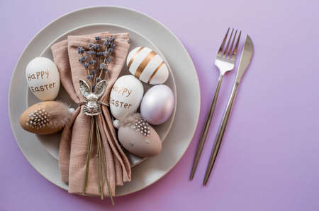 Banner. table setting. A plate with a rabbit on a napkin, lavender and Easter eggs on a fashionable background of 2022 is a veri pery. top view. The concept of a happy Easter holiday for cafes.の写真素材