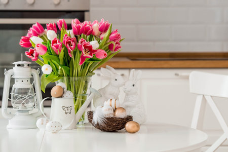 A bouquet of tulips, Easter bunnies and eggs with a golden pattern on the table. In the background is a white Scandinavian-style kitchen. beautiful greeting card. The minimal concept.の写真素材