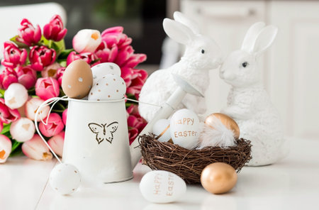 A bouquet of tulips, Easter bunnies and eggs with a golden pattern on the table. In the background is a white Scandinavian-style kitchen. beautiful greeting card. The minimal concept.の写真素材