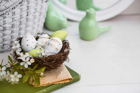 Banner. White-green eggs, cherry blossoms in a nest, an old book and porcelain birds on a white wooden table. A card festive for happy Easter Day 2022 in vintage style.の写真素材