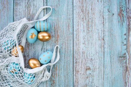 Gold, black, white, blue eggs in a string bag on a blue wooden background. geometry. The minimal concept. top view. An Easter card with a copy of the place for the text.の写真素材