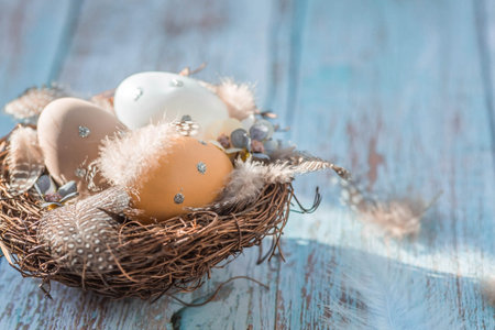 Easter eggs, feathers in a nest on a blue wooden background. The minimal concept. top view. Card...
