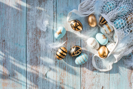 Gold, black, white, blue eggs in a string bag on a blue wooden background. geometry. The minimal concept. top view. An Easter card with a copy of the place for the text.の写真素材