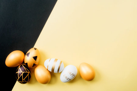 Golden, black, white easter eggs on a yellow-black background. geometry. minimal concept. view from above. Card with copy space for text.の写真素材