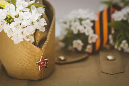 Banner for May 9. A military uniform, a cap with a star, a St. George ribbon and a cherry blossom in the background. The concept of the Great Victory Day 941-1945 and Defender of the Fatherland Day.の写真素材