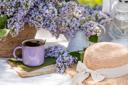 The postcard is very beautiful. A fashionable purple coffee mug, an old book, birds, a straw hat and a bouquet of purple lilac. A beautiful still life. springtime. The concept of "Good morning".の写真素材