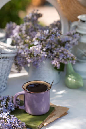 The postcard is very beautiful. A fashionable purple coffee mug, an old book, birds, a straw hat and a bouquet of purple lilac. A beautiful still life. springtime. The concept of "Good morning".の写真素材