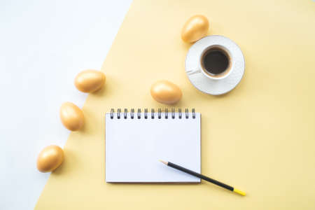 Golden easter eggs, coffee mug and notebook with place for text on on yellow background. Trendy flat lay. minimal concept.の写真素材