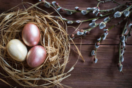 Pink and yellow Easter eggs in nest on wooden background. Minimal easter concept. Easter card with copy space for text.の写真素材