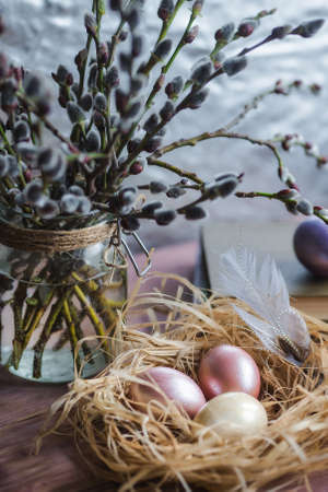 A bouquet of willow and Easter eggs in a nest on a wooden background. The concept of a happy bright Easter.の写真素材
