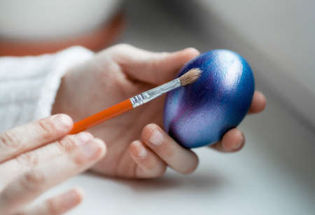 The child paints the Easter egg in blue. Egg in hand close-up. Moscow, April.の写真素材