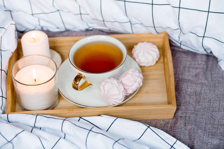 Wooden tray with tea, marshmallows and candles on the bed. White sheets with a striped blanket and pillow. Breakfast in bed.の写真素材
